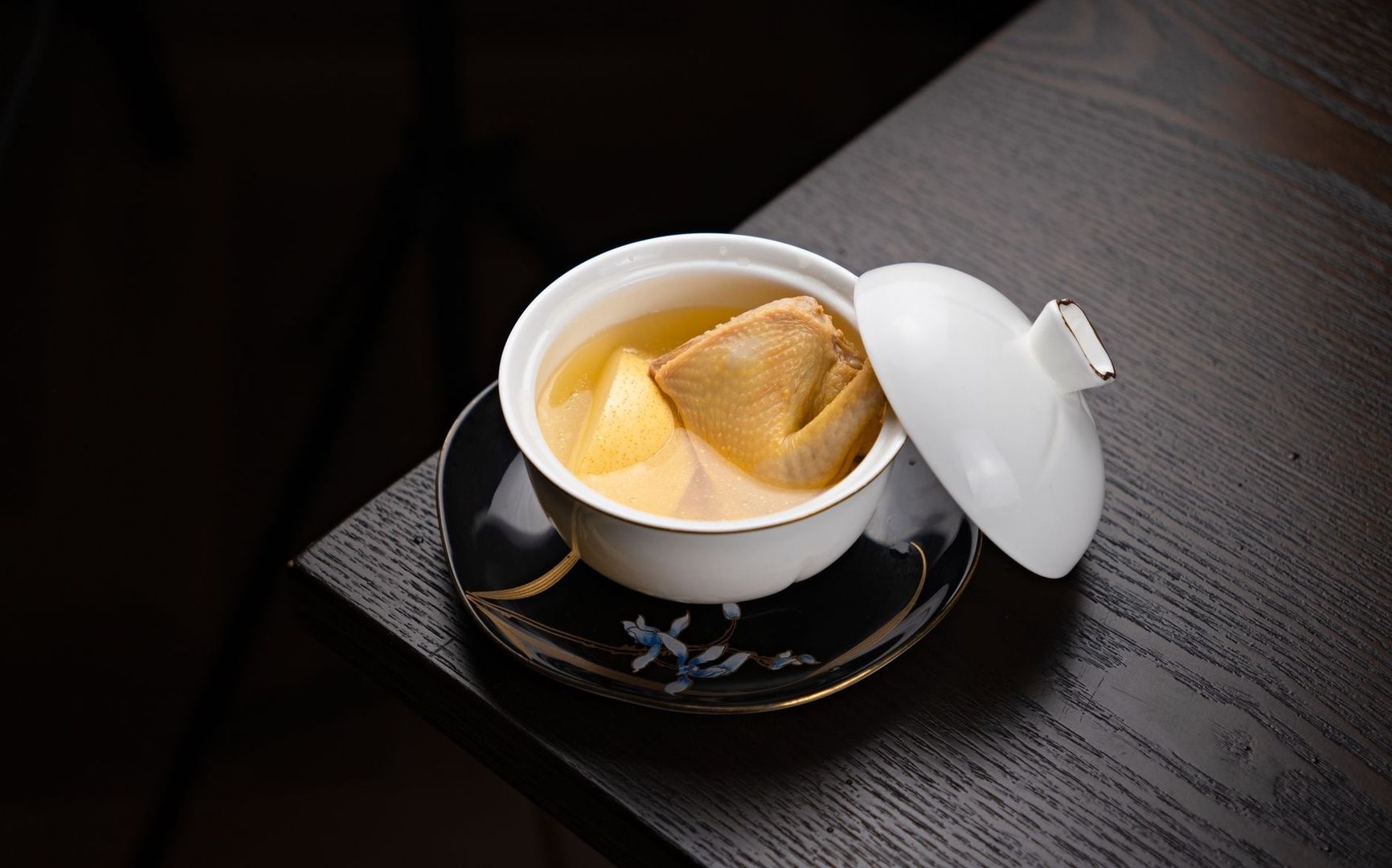 Klare goldene Bouillon mit einem Stück Geflügel in einer weißen Schale