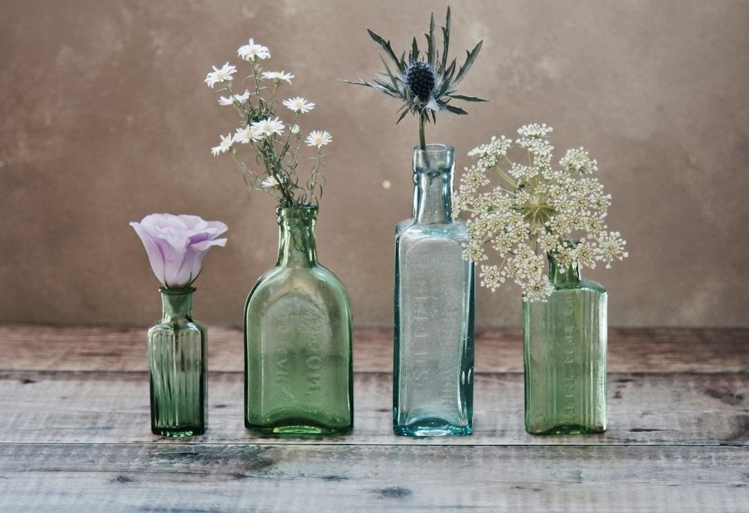 Vier Vintage-Glasflaschen mit unterschiedlichen weißen und violetten Blumen